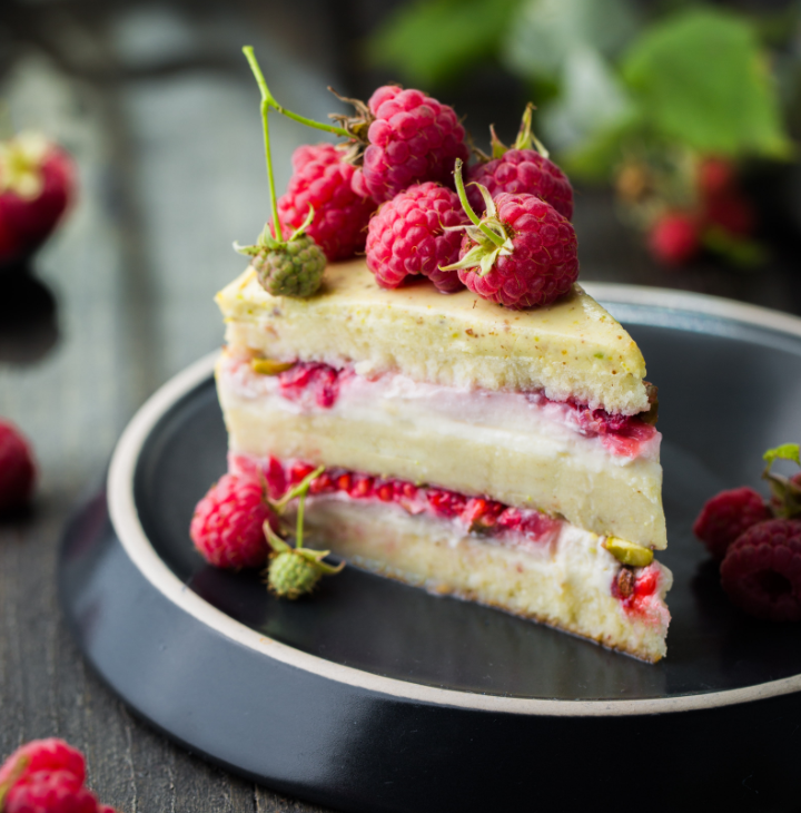 A rasperry layer cake slice with fresh rasperries on top. Served
                on a fancy plate.